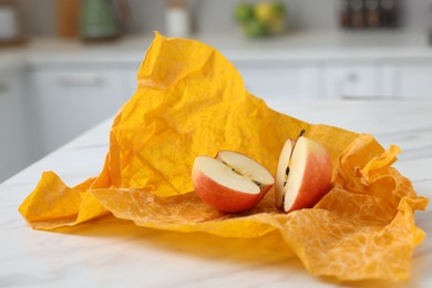 Photo of Halves of apple with orange beeswax food wrap on white table, closeup