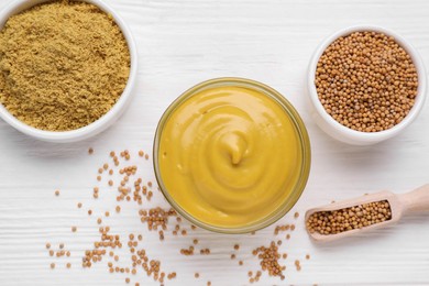 Photo of Bowl with delicious mustard, powder and seeds on white wooden table, flat lay