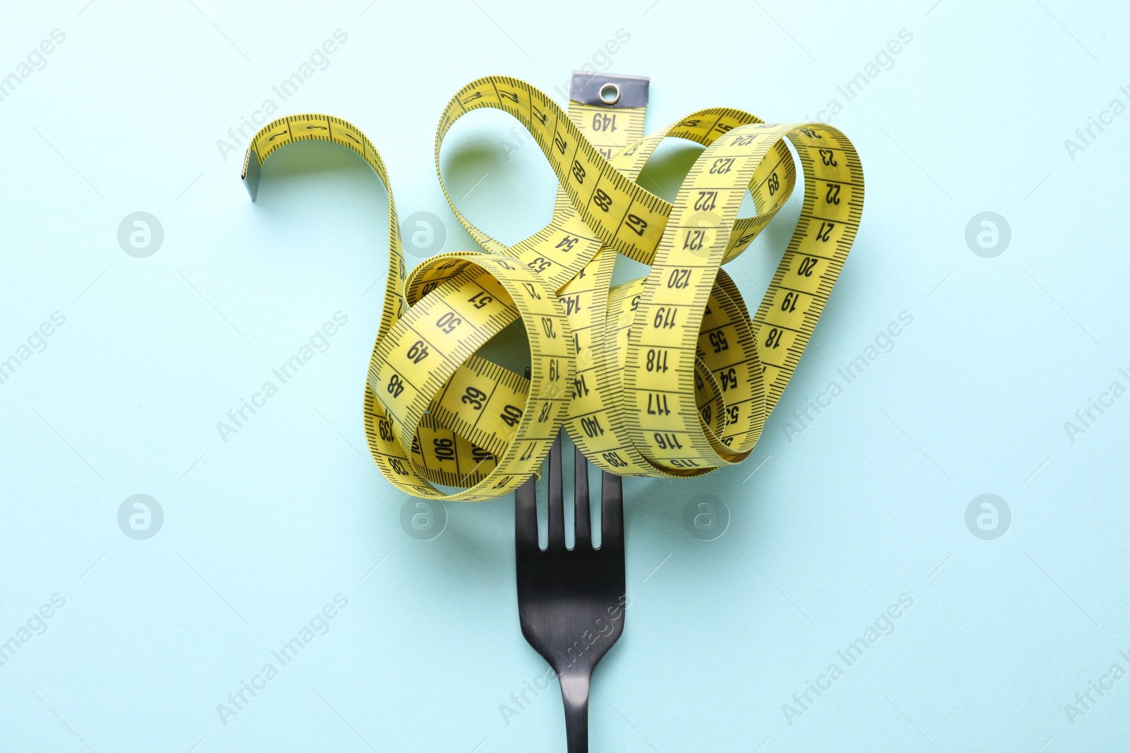 Fork with measuring tape on light blue background, top view. Diet concept Photo of Fork with measuring tape on light blue background, top view. Diet concept