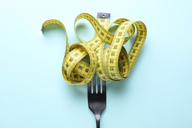 Photo of Fork with measuring tape on light blue background, top view. Diet concept