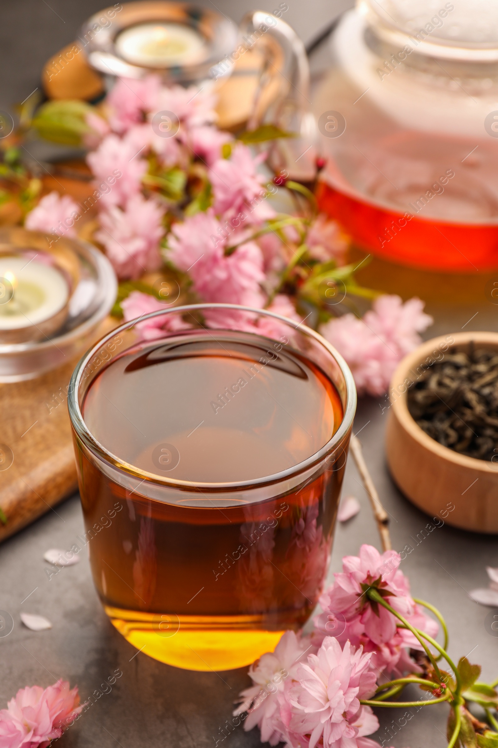 Photo of Traditional ceremony. Cup of brewed tea, teapot and sakura flowers on grey table, closeup