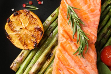 Photo of Tasty grilled salmon with asparagus, lemon and spices on plate, top view