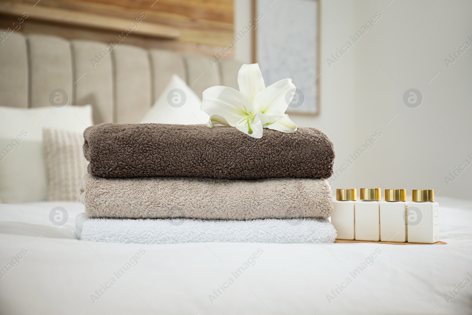 Photo of Stack of clean towels, flower and shampoo bottles on bed indoors