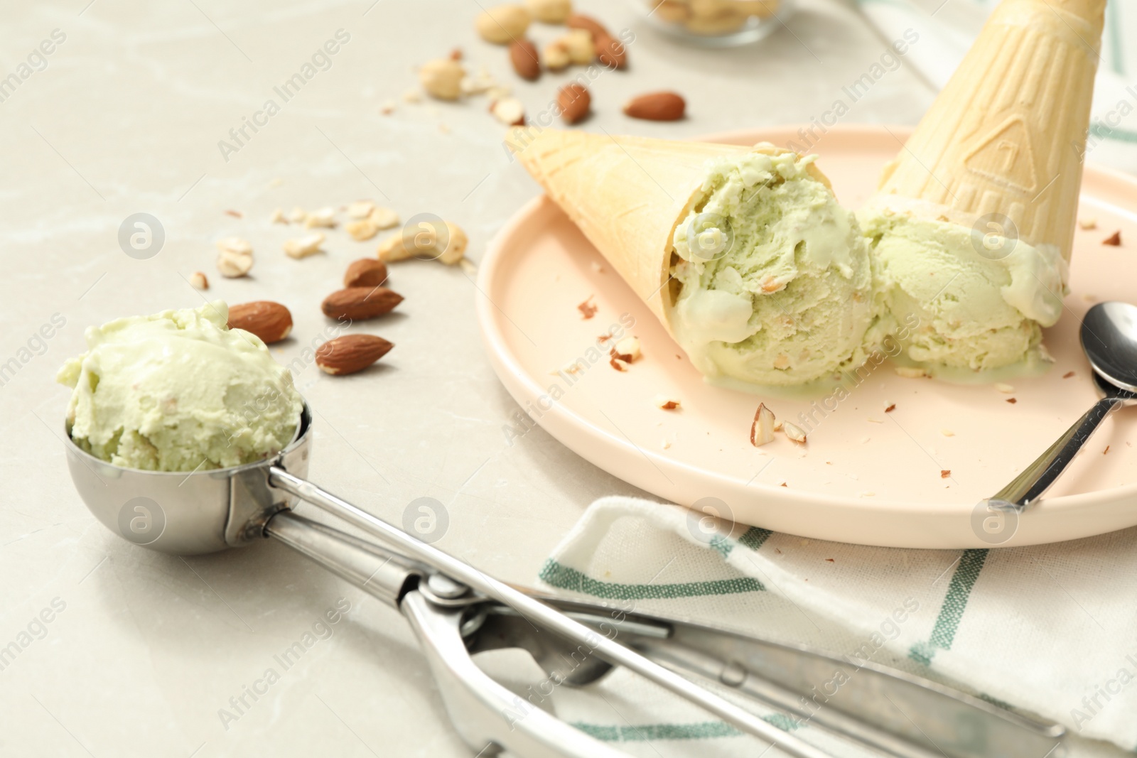 Photo of Delicious pistachio ice cream in wafer cones with chopped nuts on light table, closeup