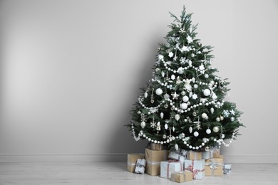 Beautiful Christmas tree and gift boxes near light grey wall in room, space for text
