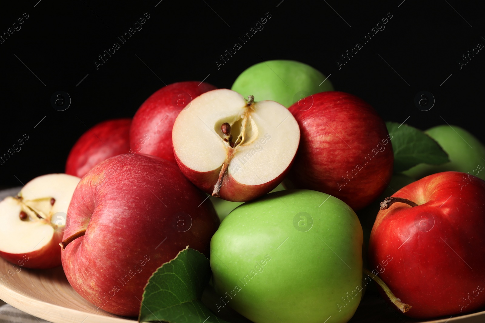 Photo of Fresh ripe apples and leaves on wooden plate against dark background, closeup