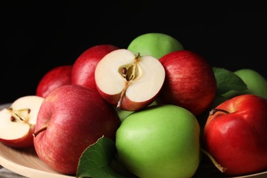 Fresh ripe apples and leaves on wooden plate against dark background, closeup