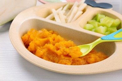 Photo of Healthy baby food. Section plate with delicious pumpkin puree and vegetables on white wooden table, closeup