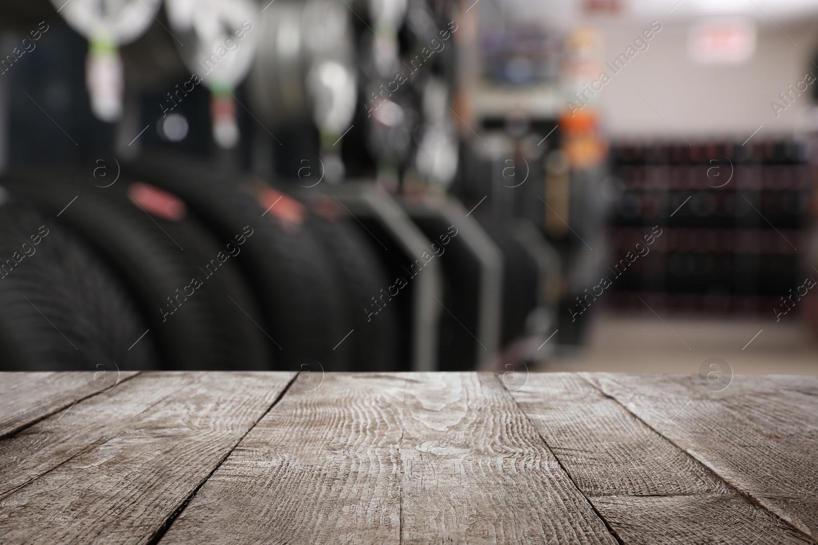 Image of Empty wooden surface and blurred view of car tires in auto store, closeup. Space for text 