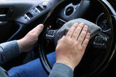 Photo of Man cleaning steering wheel with rag in car, closeup