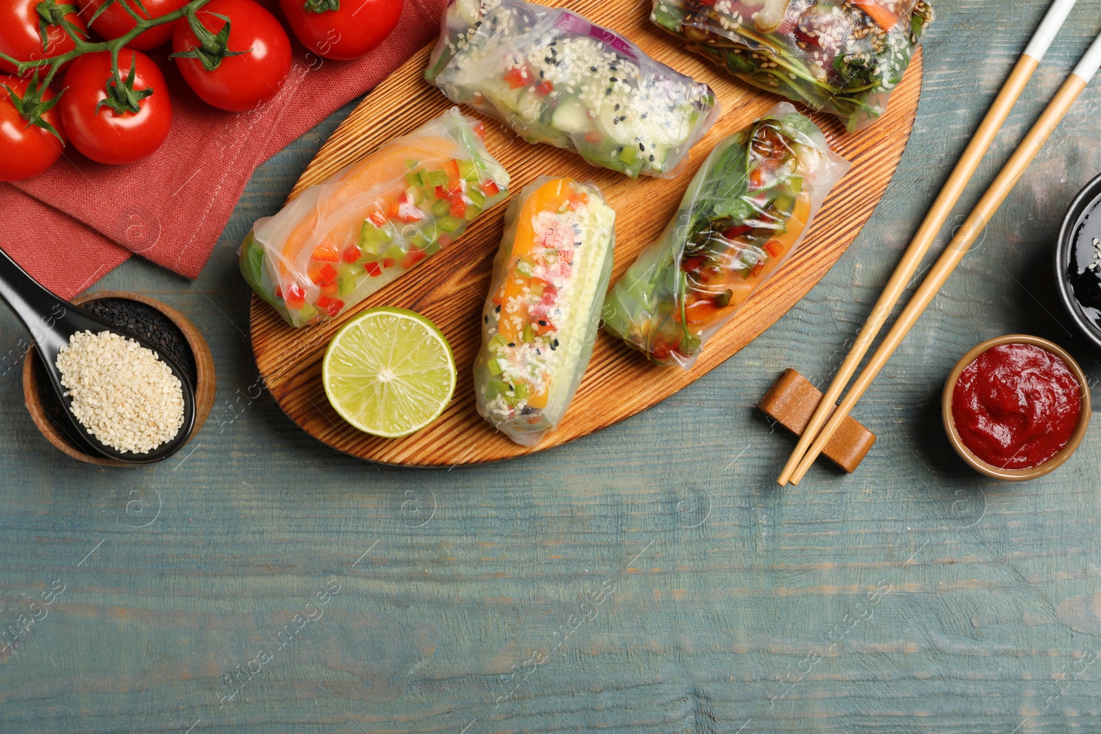Photo of Many different delicious rolls wrapped in rice paper on blue wooden table, flat lay. Space for text