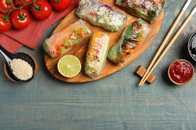 Photo of Many different delicious rolls wrapped in rice paper on blue wooden table, flat lay. Space for text