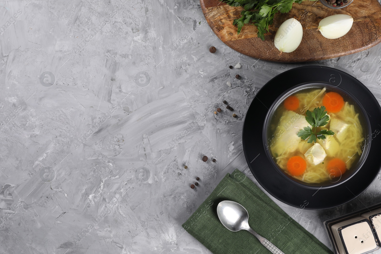 Photo of Tasty chicken soup with noodles, carrot and parsley in bowl served on grey textured table, flat lay. Space for text
