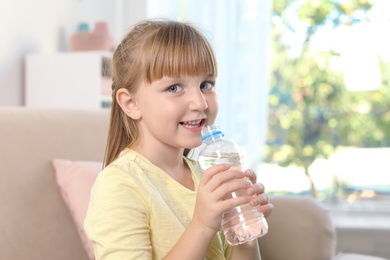 Photo of Cute little girl holding bottle with water indoors