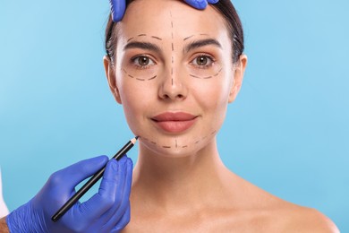 Photo of Doctor drawing marks on woman's face for cosmetic surgery operation against light blue background