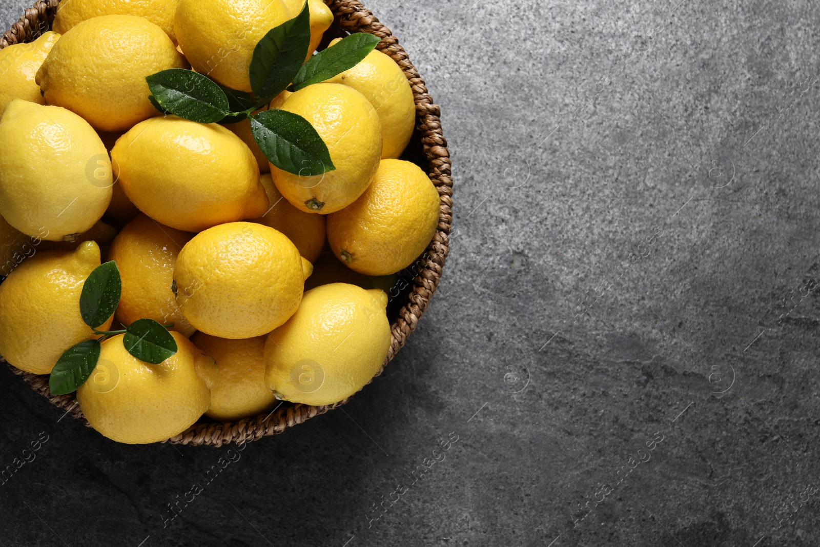 Photo of Fresh lemons in wicker basket on grey table, top view. Space for text