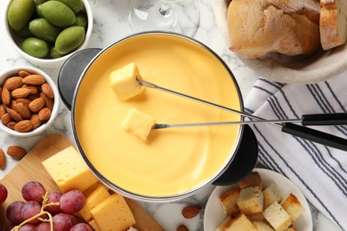 Photo of Pot of tasty cheese fondue and snacks on white marble table, flat lay