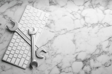 Photo of Keyboard and spanners on white marble table, flat lay with space for text. Concept of technical support