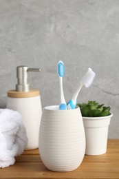 Photo of Plastic toothbrushes in holder, towel, potted plant and cosmetic product on wooden table