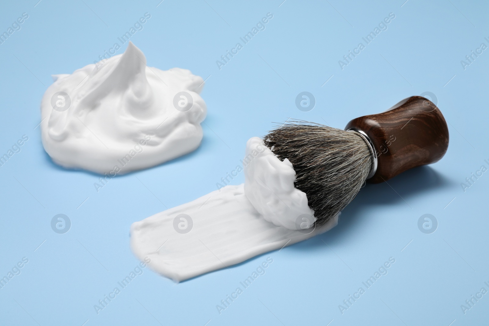 Photo of Brush with shaving foam on light blue background