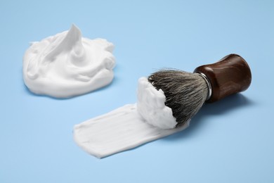 Photo of Brush with shaving foam on light blue background
