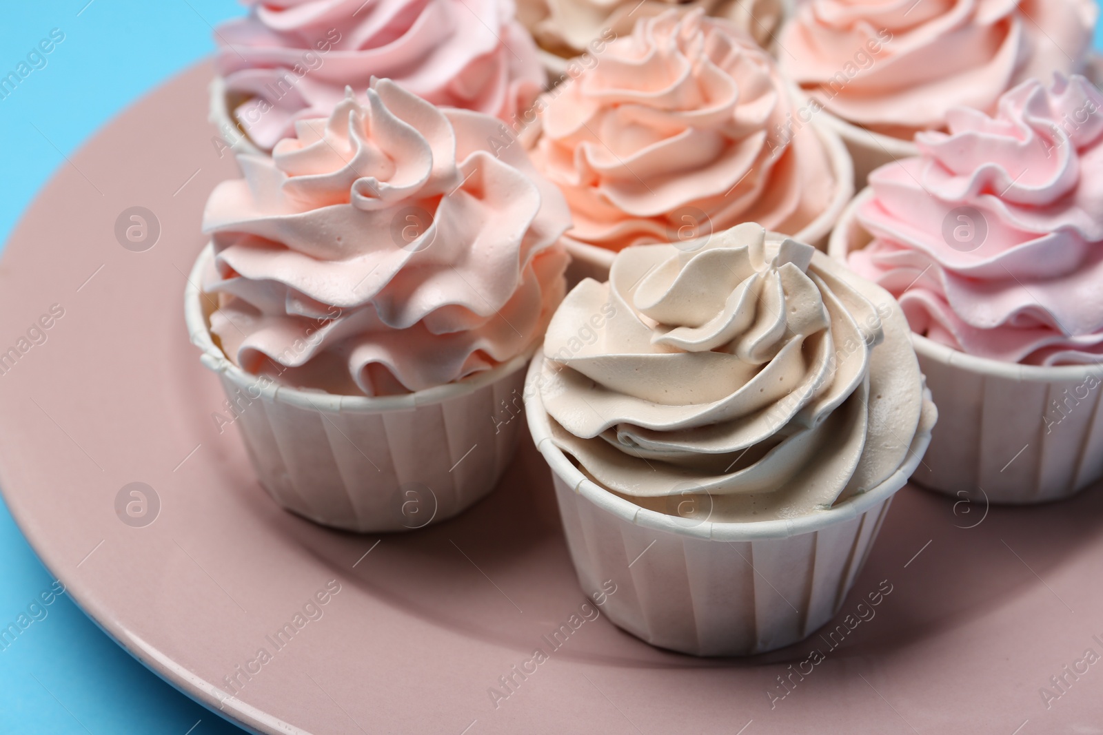 Photo of Plate with tasty cupcakes on light blue background, closeup