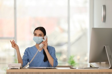 Photo of Receptionist with protective mask talking on phone at countertop in hospital