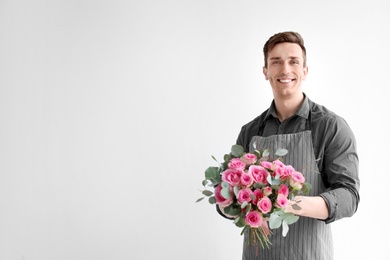 Male florist holding bouquet of beautiful flowers on light background