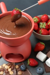Dipping fresh strawberry in fondue pot with melted chocolate at grey table, closeup