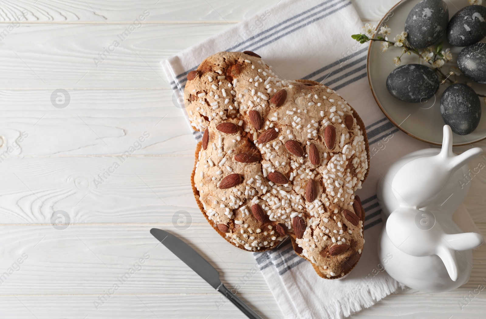 Photo of Delicious Italian Easter dove cake (Colomba di Pasqua), decorated eggs and bunny figures on white wooden table, flat lay. Space for text