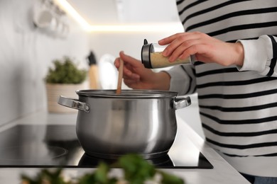 Woman adding spices into pot with soup in kitchen, closeup