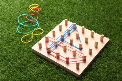 Wooden geoboard with boat made of rubber bands on artificial grass. Educational toy for motor skills development