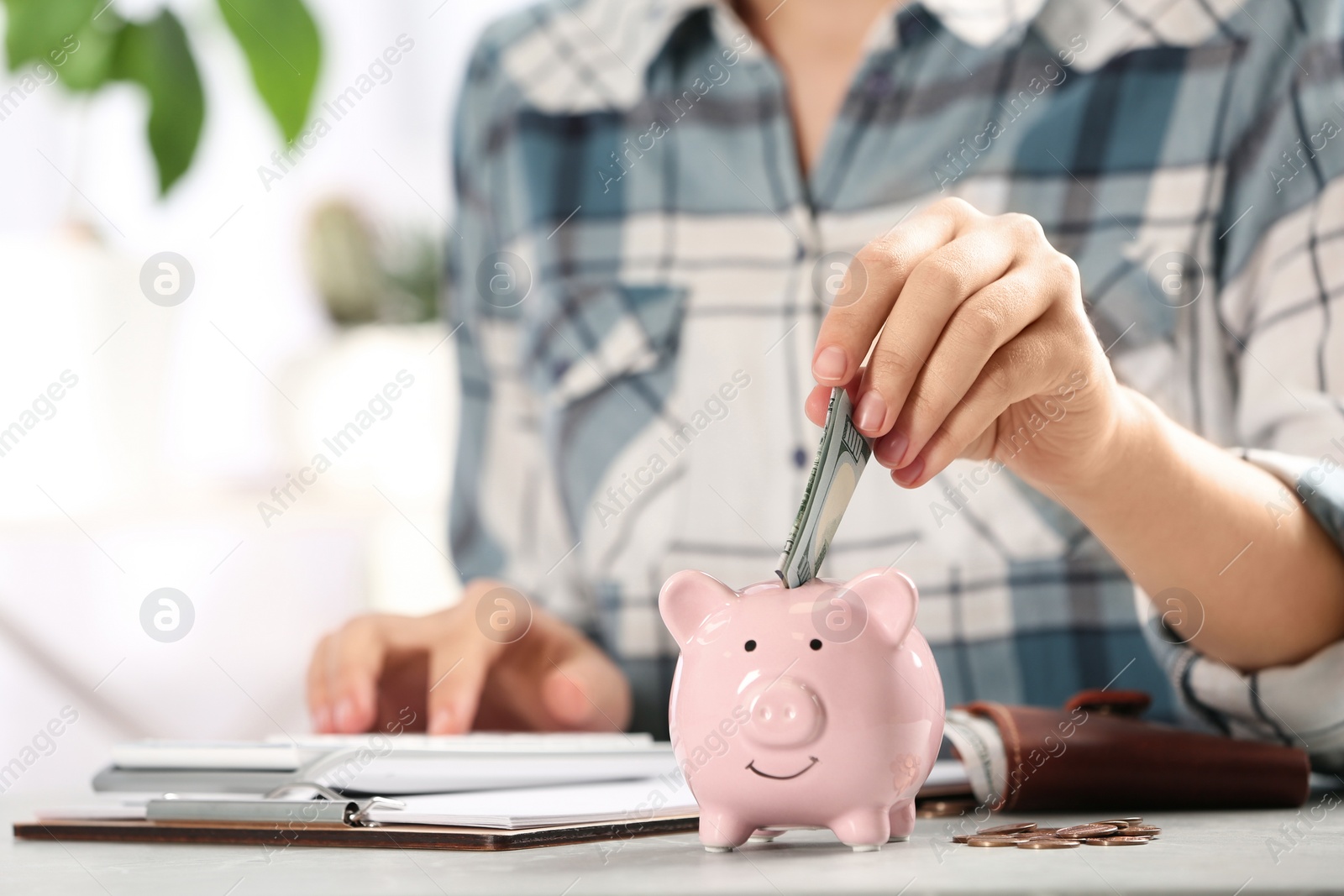 Photo of Woman putting money into piggy bank at table indoors, closeup