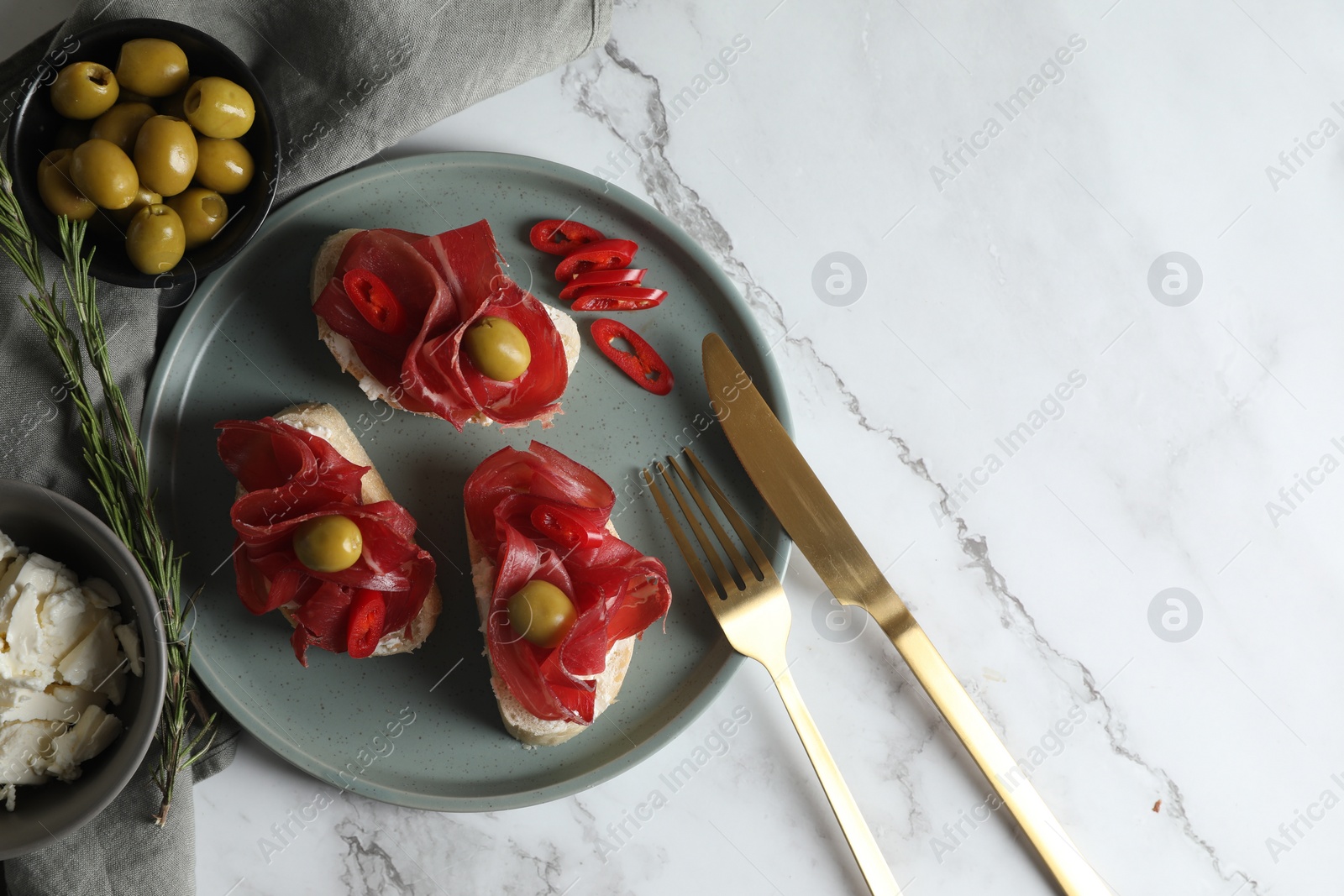 Photo of Delicious sandwiches with bresaola, cream cheese and olives served on white marble table, flat lay. Space for text