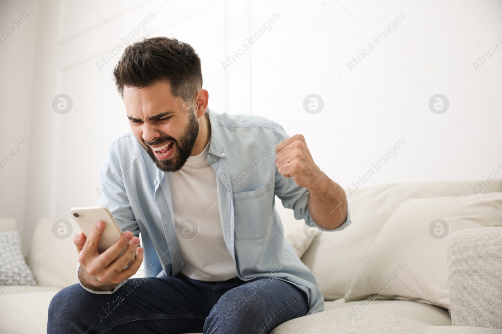 Photo of Emotional young man with mobile phone at home. Online hate concept