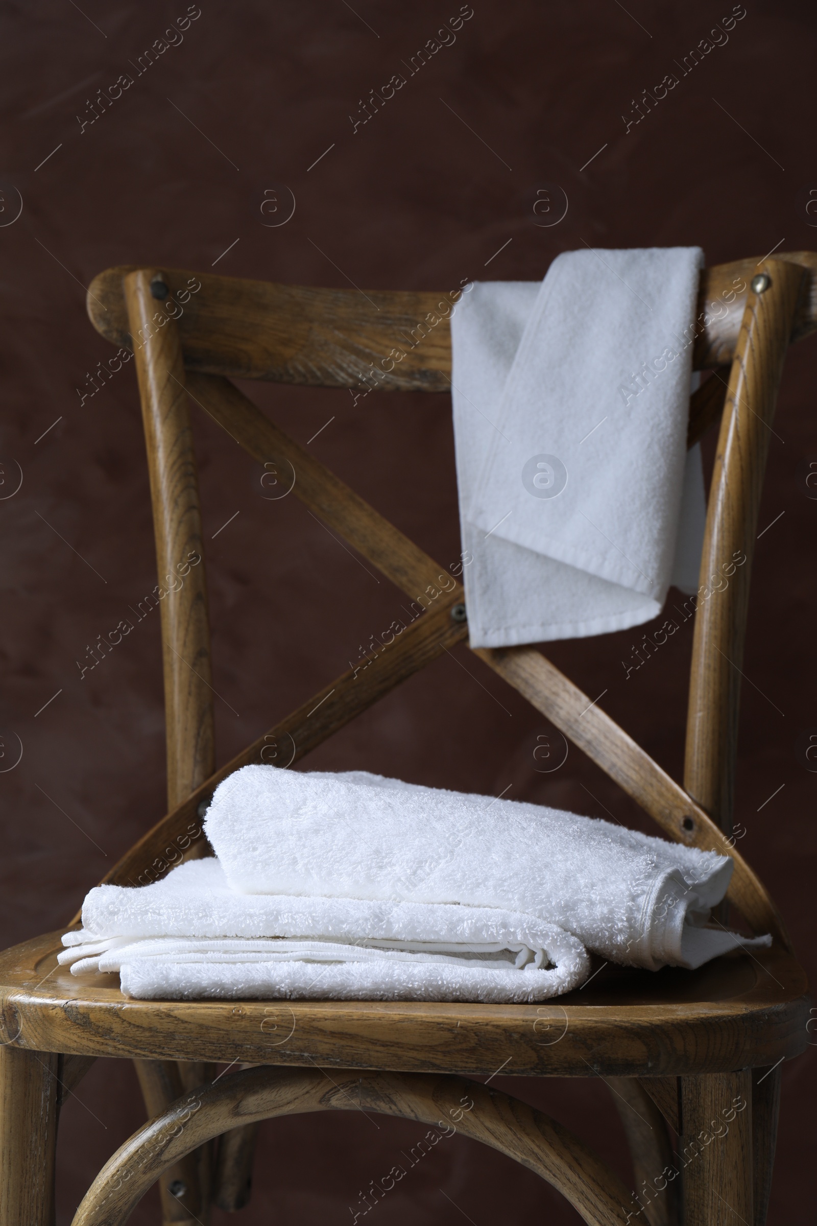 Photo of White terry towels on wooden chair against brown background