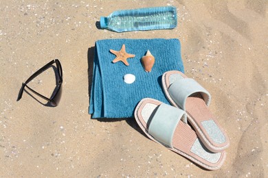 Photo of Blue towel, stylish sunglasses, slippers and bottle of water on sand. Beach accessories