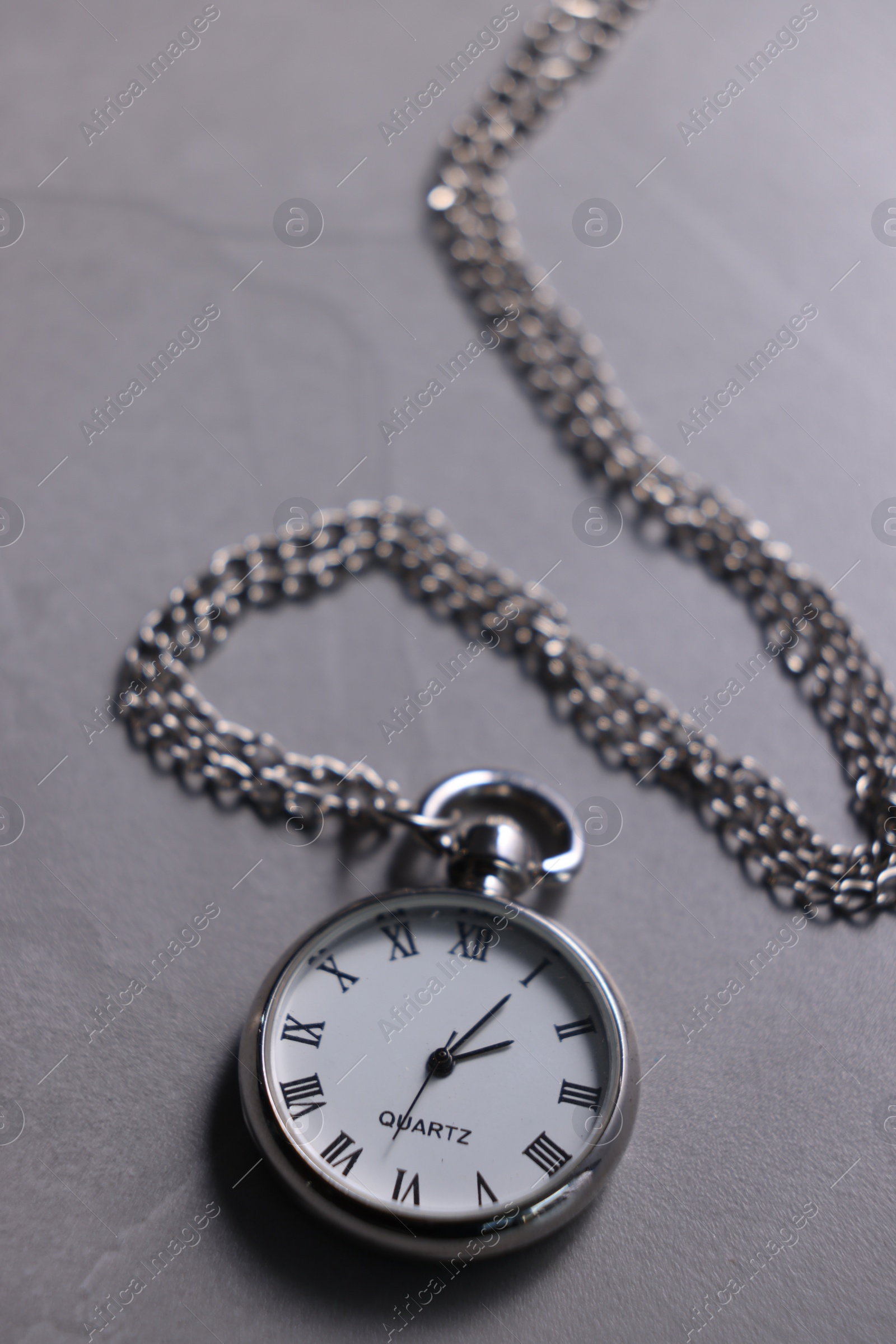 Photo of Silver pocket clock with chain on grey table, closeup