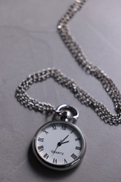 Silver pocket clock with chain on grey table, closeup