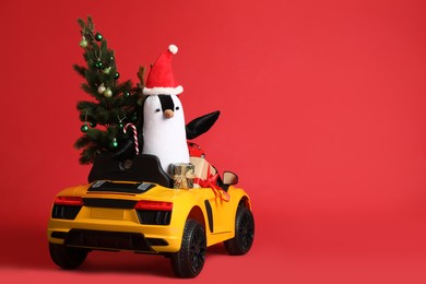 Photo of Child's electric car with toys, gift boxes and Christmas tree on red background, space for text