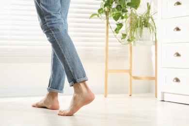 Photo of Barefoot woman walking on white parquet at home, closeup. Heated floor