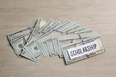 Photo of Paper with word Scholarship and banknotes on wooden table, flat lay