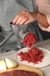 Woman making beef mince with manual meat grinder at light wooden table, closeup