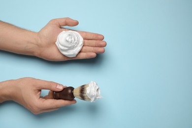 Man holding shaving foam and brush on light blue background, top view. Space for text