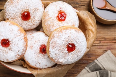 Photo of Delicious donuts with jelly and powdered sugar in baking dish on wooden table, flat lay