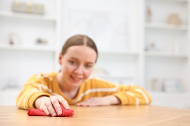 Woman cleaning wooden table with rag indoors, selective focus