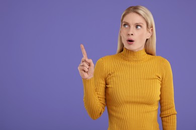 Surprised woman pointing at something on violet background, space for text