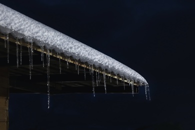 Photo of House roof with snow and icicles at night, closeup