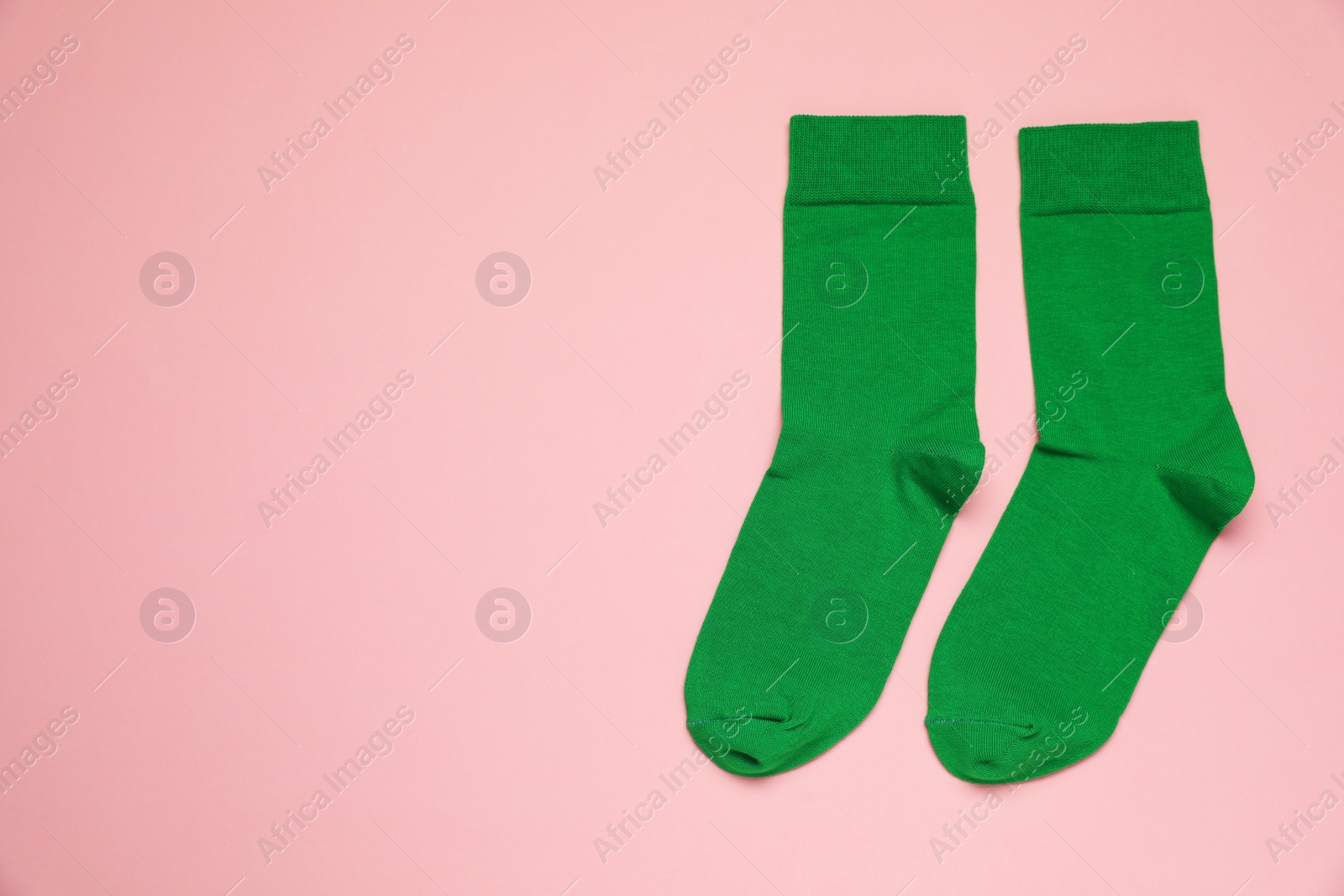 Photo of Green socks on pink background, flat lay. Space for text
