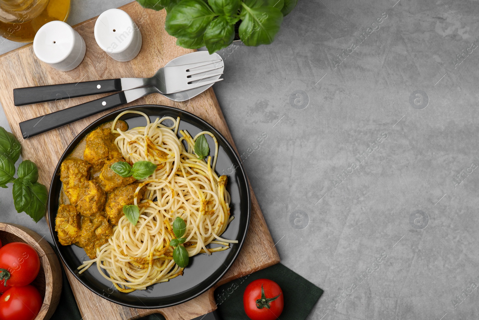 Photo of Delicious pasta and chicken with curry sauce served on grey table, flat lay. Space for text